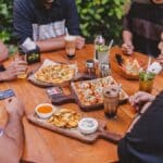 a group of people sitting around a table with pizzas and drinks