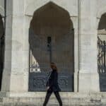 person in suit jacket walking on front of black gate