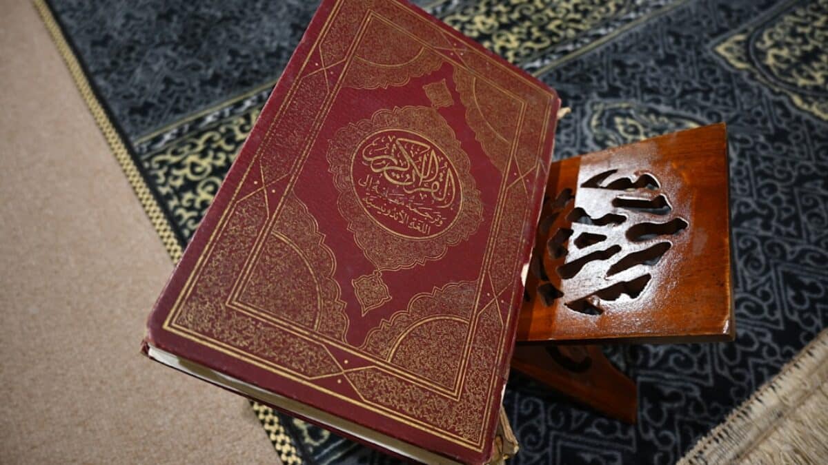 The quran sits open on a wooden book stand.